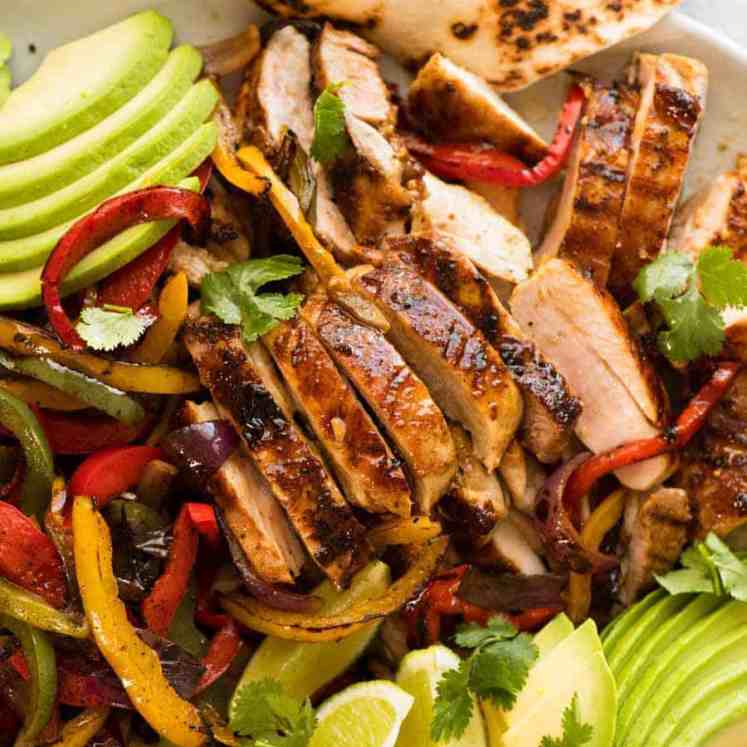 Close up of sliced Chicken Fajitas alongside charred peppers, avocado and warm tortillas, ready to be served.