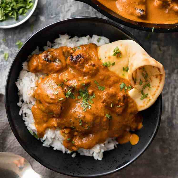 Overhead photo of chicken tikka masala on basmati rice in a dark rustic bowl with a piece of naan wedged in on the side.