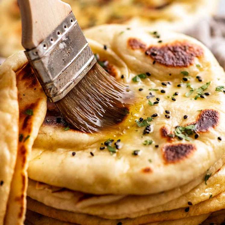 Brushing melted garlic butter on a freshly cooked naan