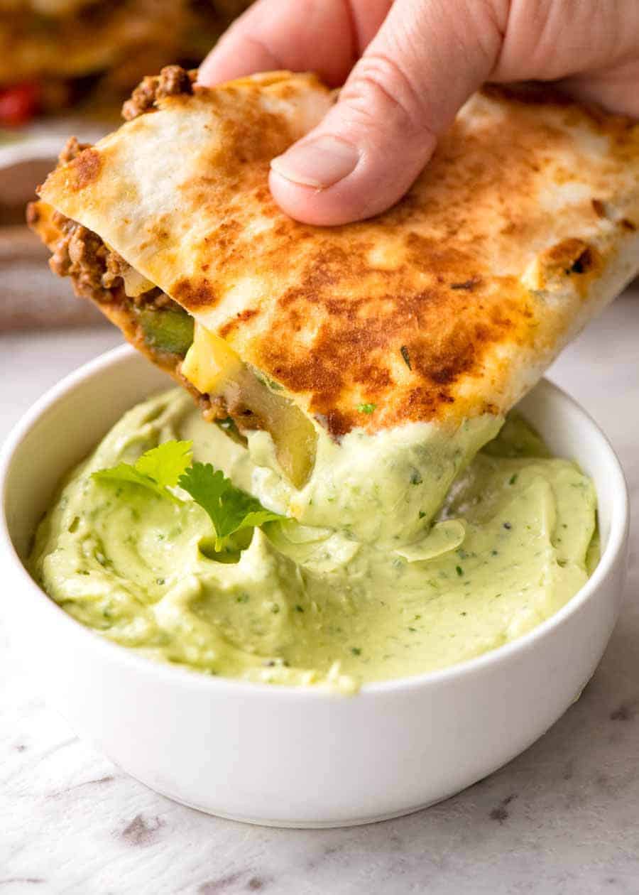 Quesadilla being dipped into avocado dipping sauce