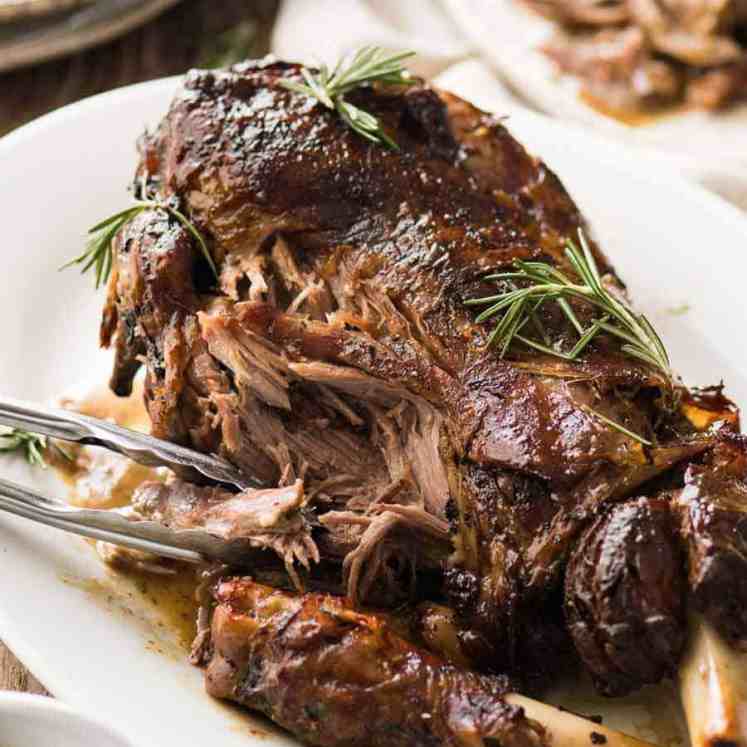 Slow Roast Leg of Lamb on a white plate with part of the meat pried off to show how tender it is