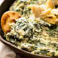 Close up of ritz cracker scooping up Spinach Artichoke Dip in a rustic black dish